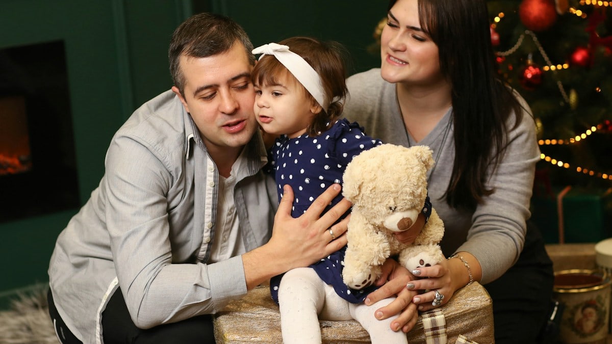 a man, woman and child sitting in front of a christmas tree